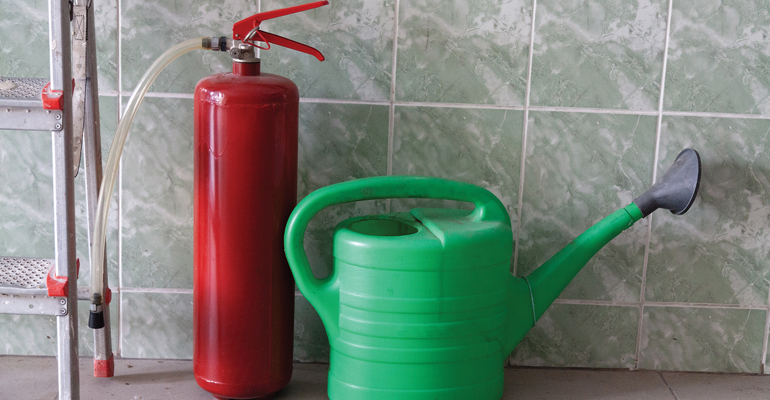 &ldquo;Watering can and fire extinguisher stand in front of wall&rdquo;