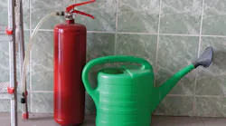 “Watering can and fire extinguisher stand in front of wall”