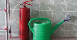 “Watering can and fire extinguisher stand in front of wall” “Watering can and fire extinguisher stand in front of wall”