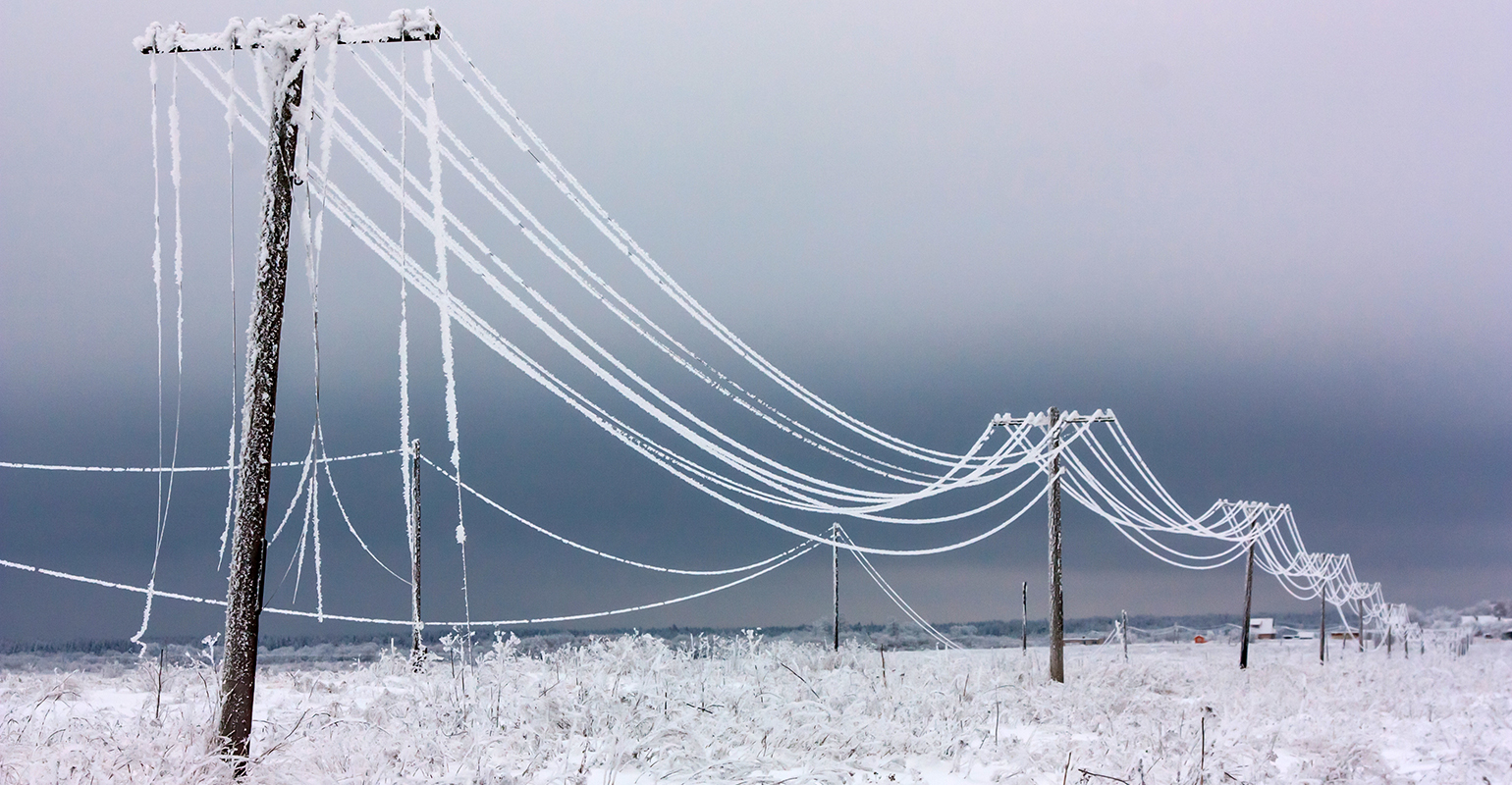 Broken phase electrical power lines with hoarfrost on the wooden electric poles on countryside in the winter after storm.