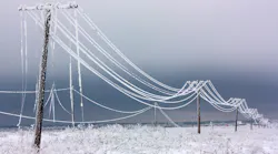 Broken phase electrical power lines with hoarfrost on the wooden electric poles on countryside in the winter after storm.