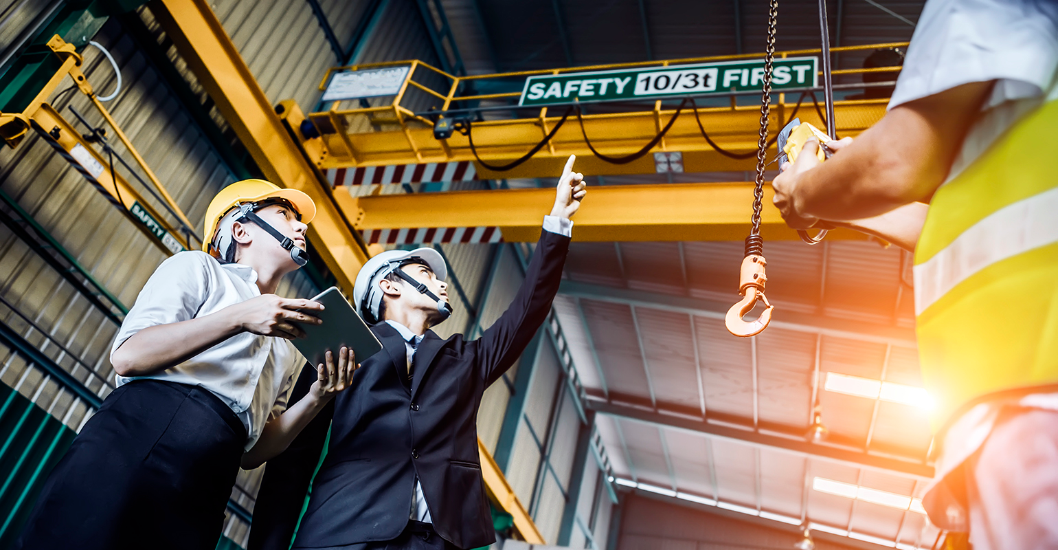 Engineer and his assistant looking up to the crane in factory shop floor.