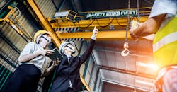 Engineer and his assistant looking up to the crane in factory shop floor. Engineer and his assistant looking up to the crane in factory shop floor.