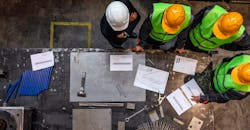 Factory workers review plans together. Factory workers review plans together.