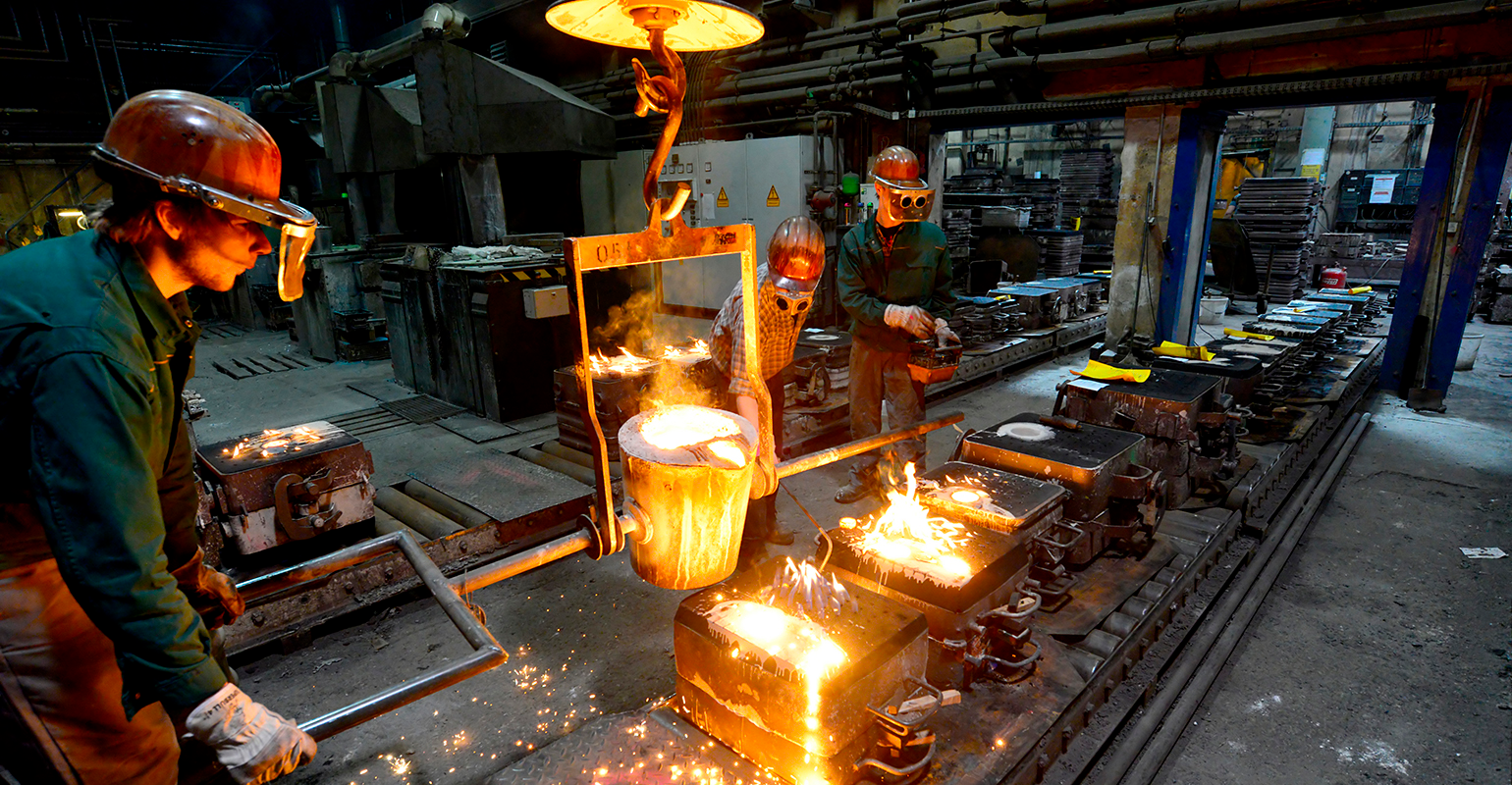 Workers in a foundry casting a metal workpiece; safety at work; teamwork.