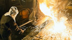 Metalcasting worker pours ladle to fill mold. Metalcasting worker pours ladle to fill mold.