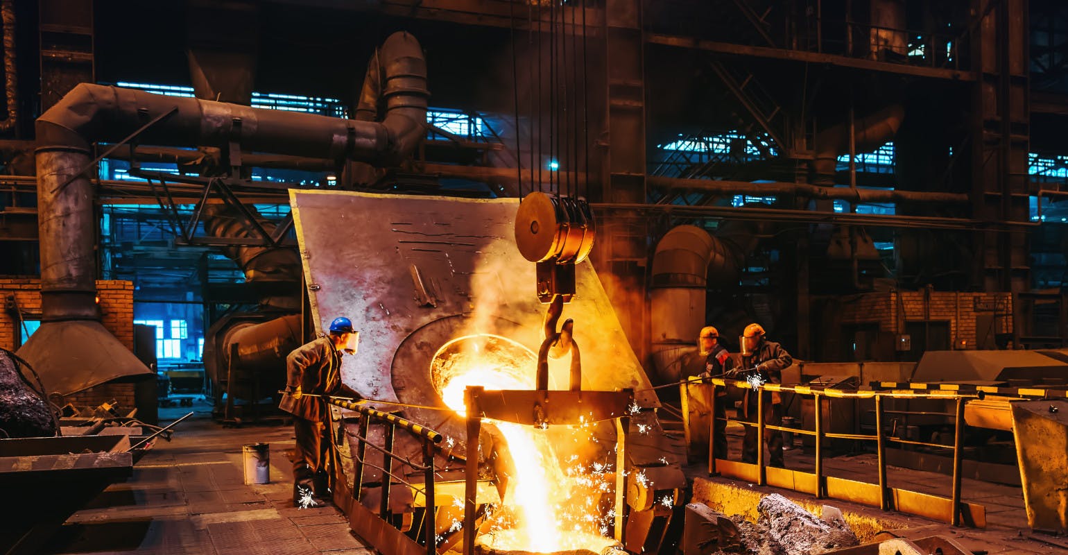 Foundry workshop interior, molten iron pouring from furnace into ladle as workers control the process.