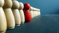 Leadership development concept: A line of wooden pegs shaped like people. One, painted red, stands out.