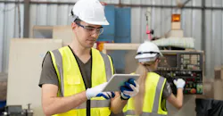 Engineer uses tablet while behind co-worker operates CNC machine.